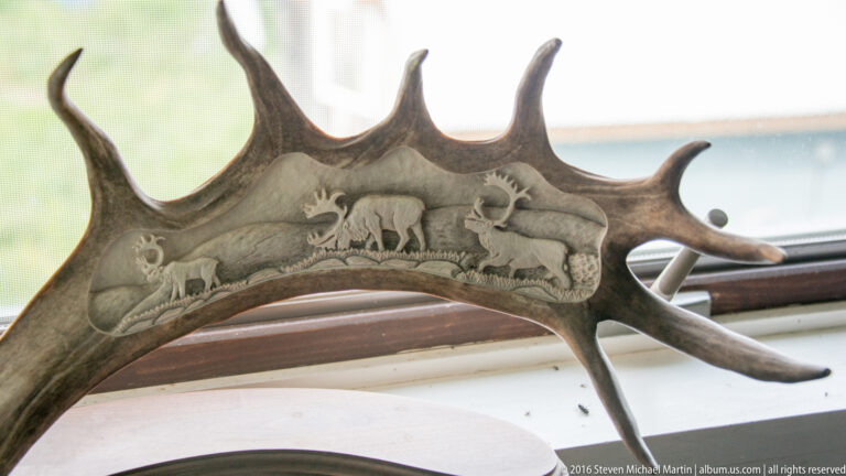 A curved antler section engraved with small animal figures and landscape details rests near a window.