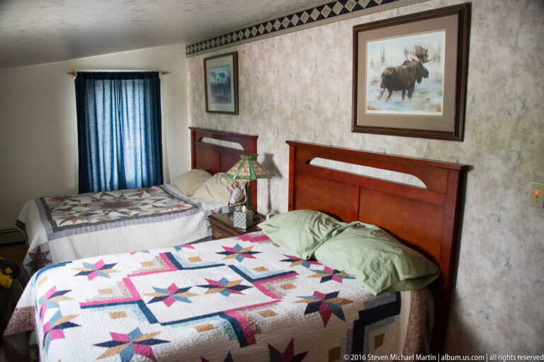 Two beds with patterned quilts and wooden headboards sit beneath framed wildlife art in a bedroom.