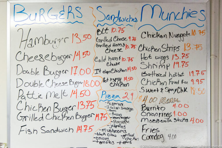 Handwritten whiteboard menu with burger, sandwich, snack, and pizza listings.