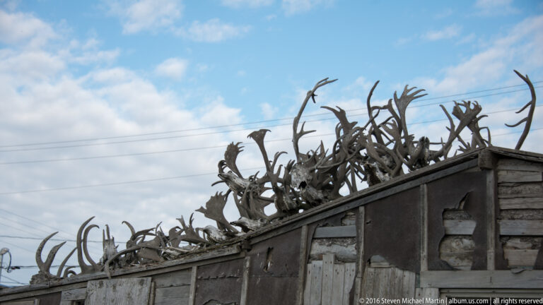 A dense row of branching antlers lines a timber roof edge against a partly cloudy sky.