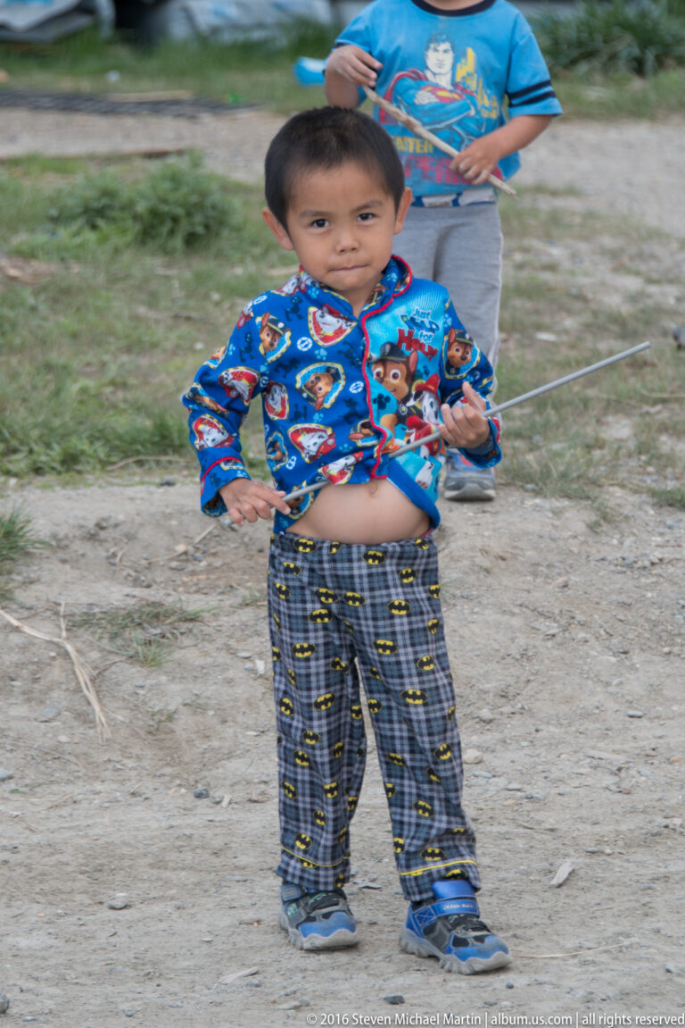 A child in a bright blue patterned shirt holds a thin line, with another child partly visible behind.