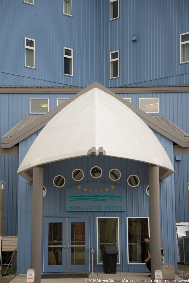 A white canopy shelters the glass entrance to the blue Nullagvik Hotel, with oval windows above.