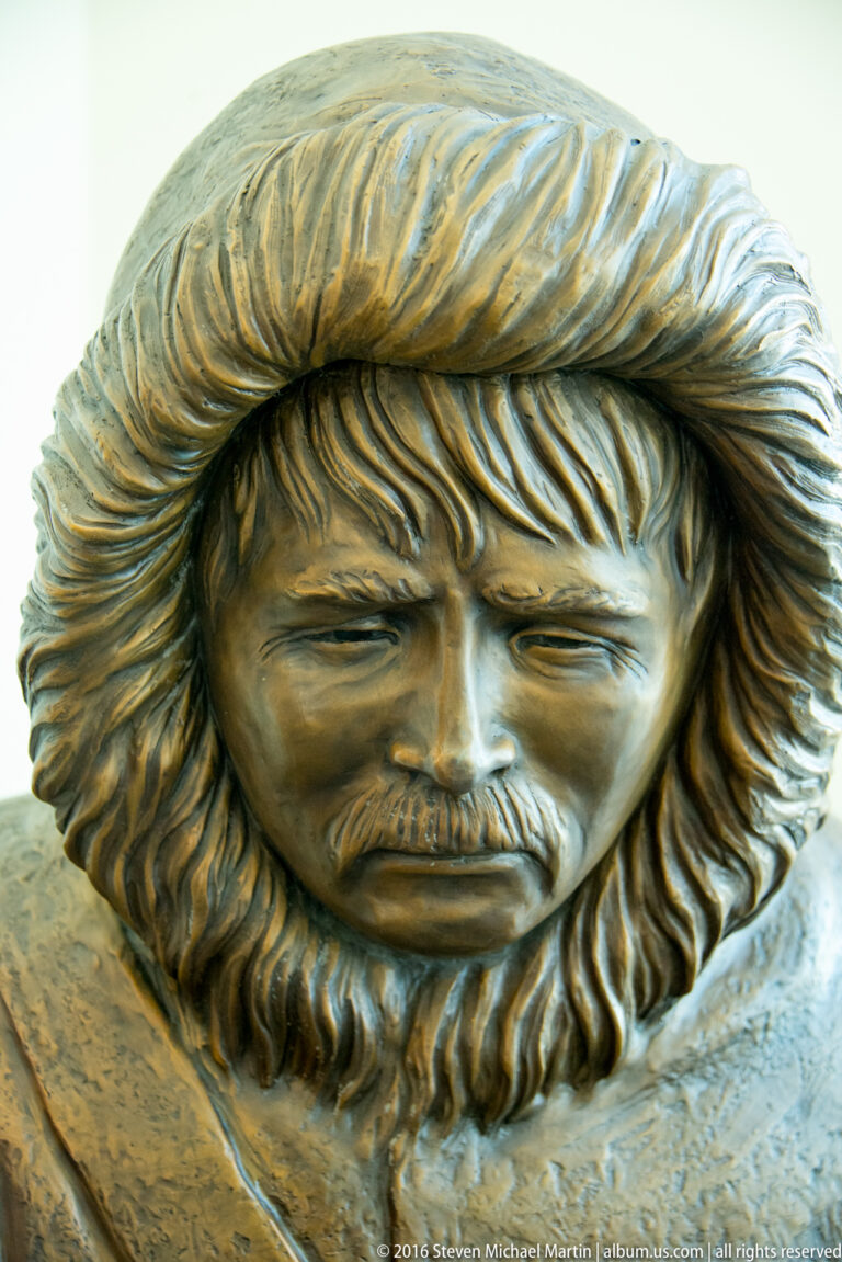 A sculpted bearded male face with long textured hair fills the frame.