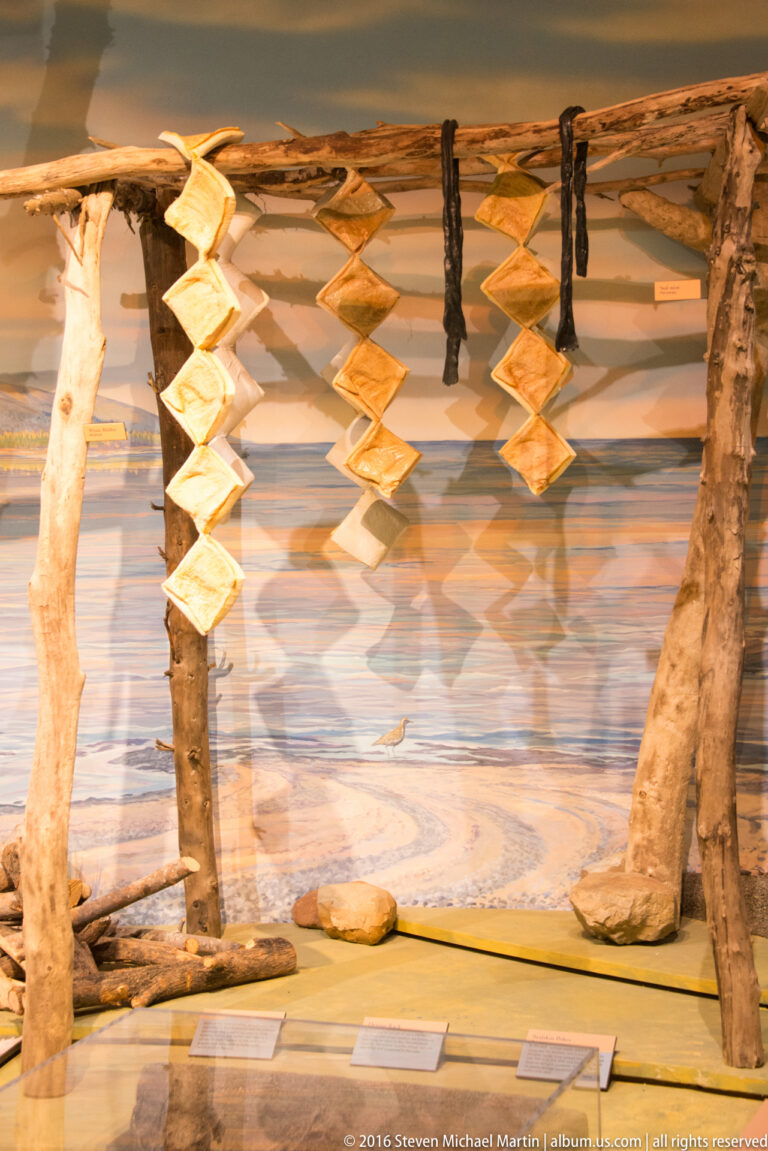 Diamond-shaped pieces hang in repeated rows between wooden posts against a landscape backdrop.