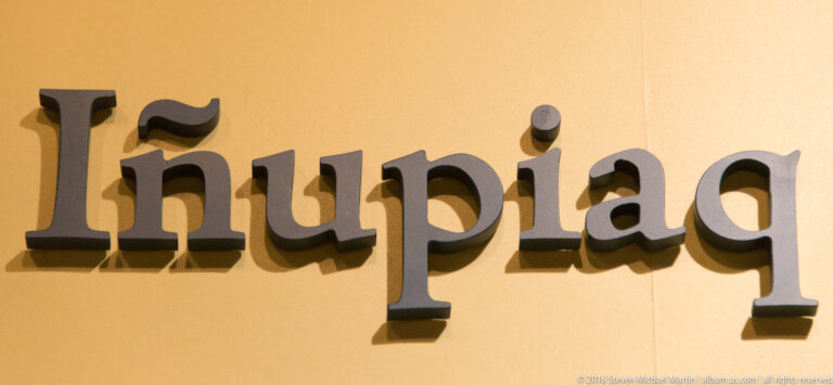 Large dimensional letters spelling “Iñupiaq” cast distinct shadows on a plain yellow interior wall.