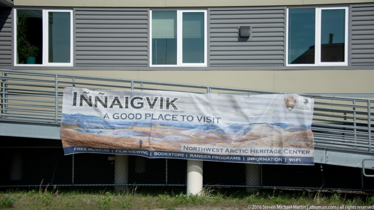 A banner on a gray building reads “Innaagvik — A Good Place to Visit” and names the Northwest Arctic Heritage Center.