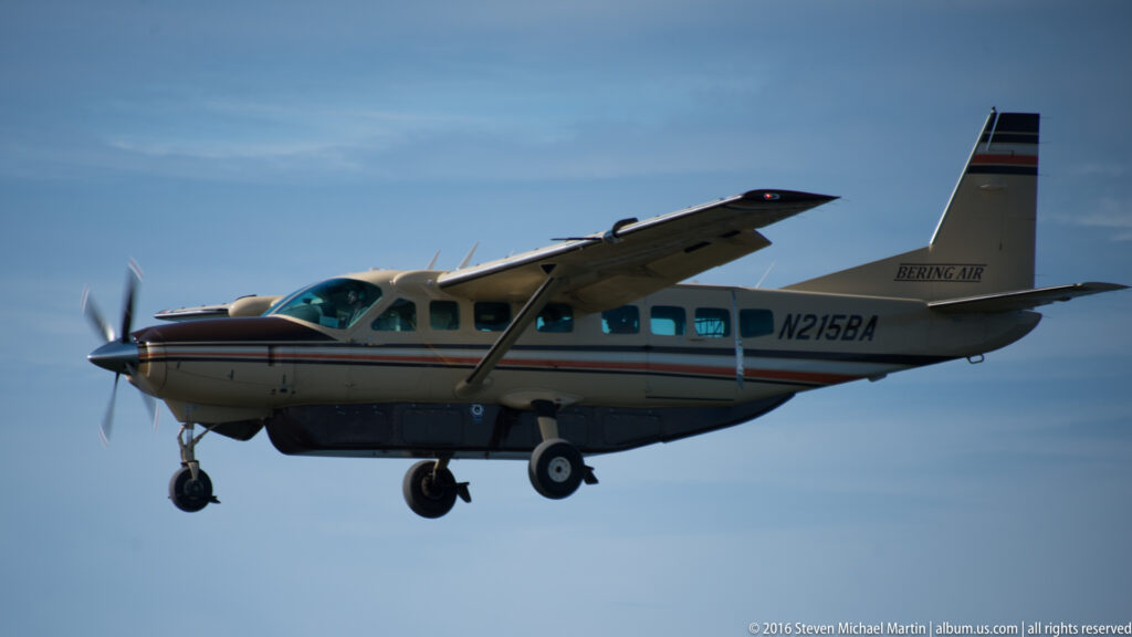 A single-engine propeller airplane flies with its landing gear extended against a blue sky.