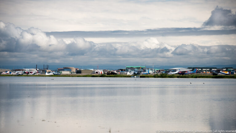 A low settlement lines the far shore of a calm lagoon beneath layered clouds.