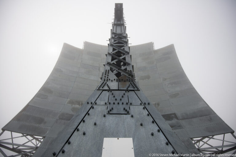 A central lattice feed tower and triangular base stand beneath a broad segmented reflector.