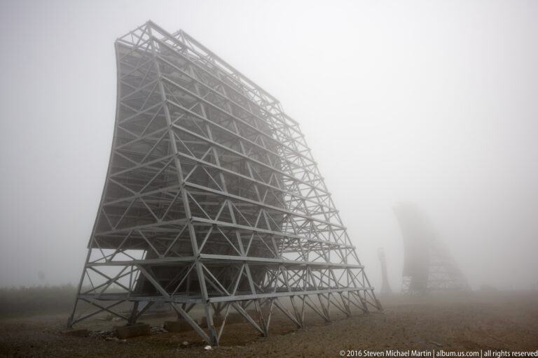 Steel lattice braces support the rear of a curved White Alice reflector in fog.