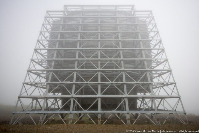 A rectangular lattice of cross-braces supports a White Alice reflector on a foggy ridge.