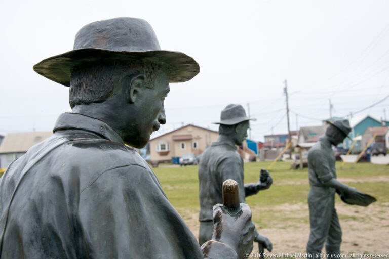Bronze miners gather around a trough, with houses and utility lines behind the sculpture.
