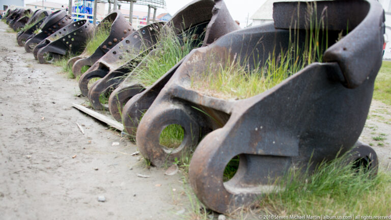 Rusted curved iron buckets lie beside a gravel path, with grass growing through the nearest one.