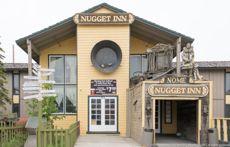 The yellow Nugget Inn facade has two name signs, a circular feature, rooftop figures, and a signpost.