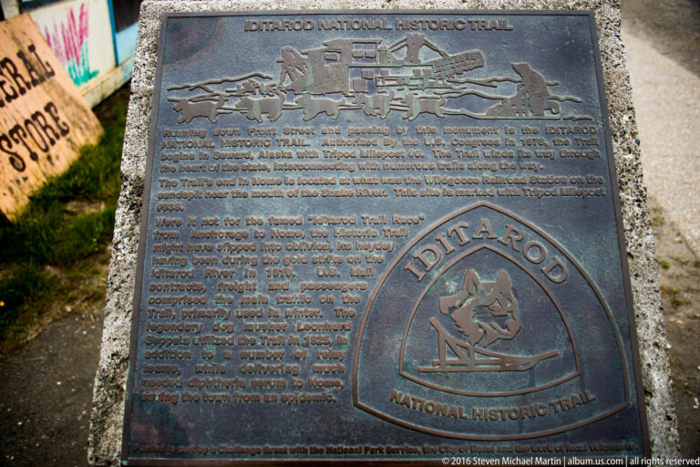 A bronze Iditarod National Historic Trail plaque shows a sled team in relief above explanatory text.