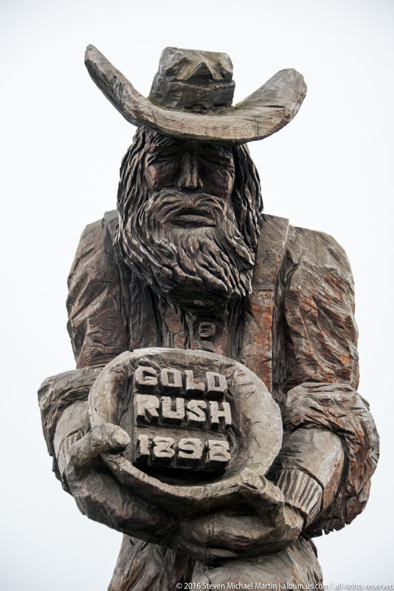 A bearded wooden figure in a broad hat holds an oval sign reading “Cold Fish.”