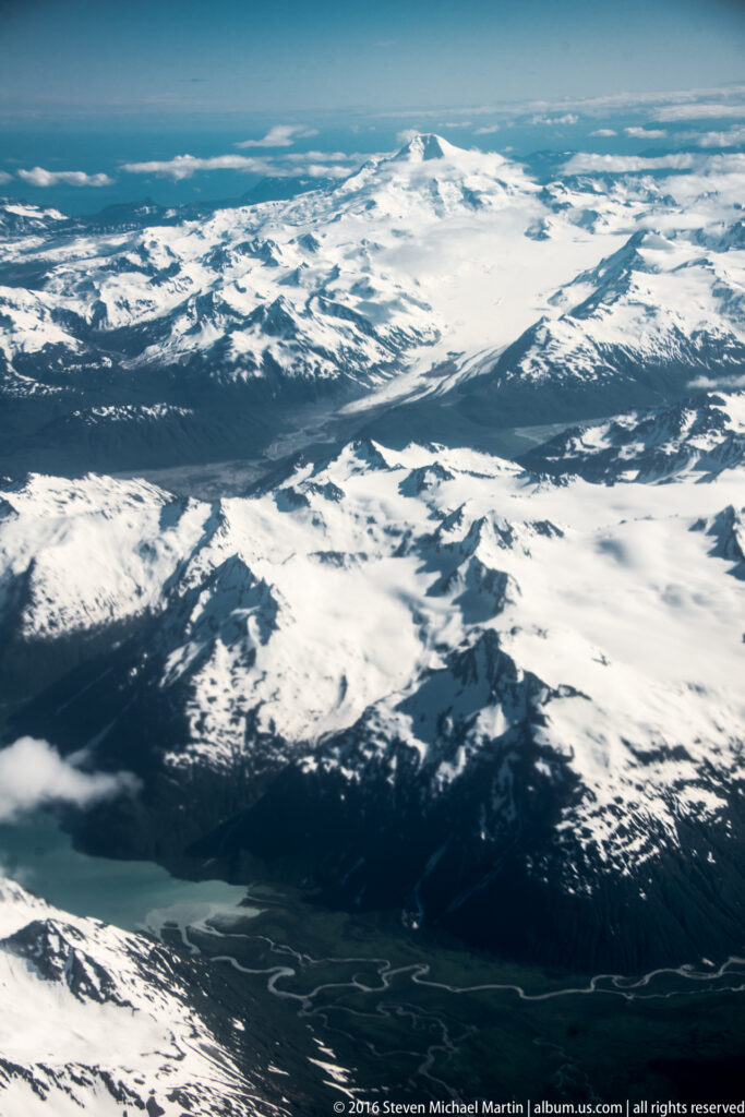 Snow-covered uplands descend toward dark ridges and a winding network of river channels.