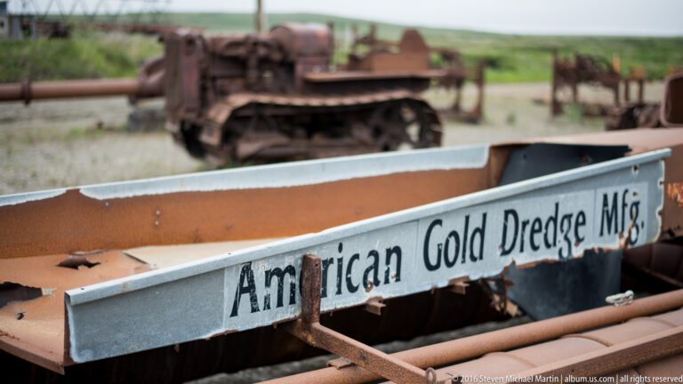A metal plate reading “American Gold Dredge Mfg.” is attached to rusted machinery.