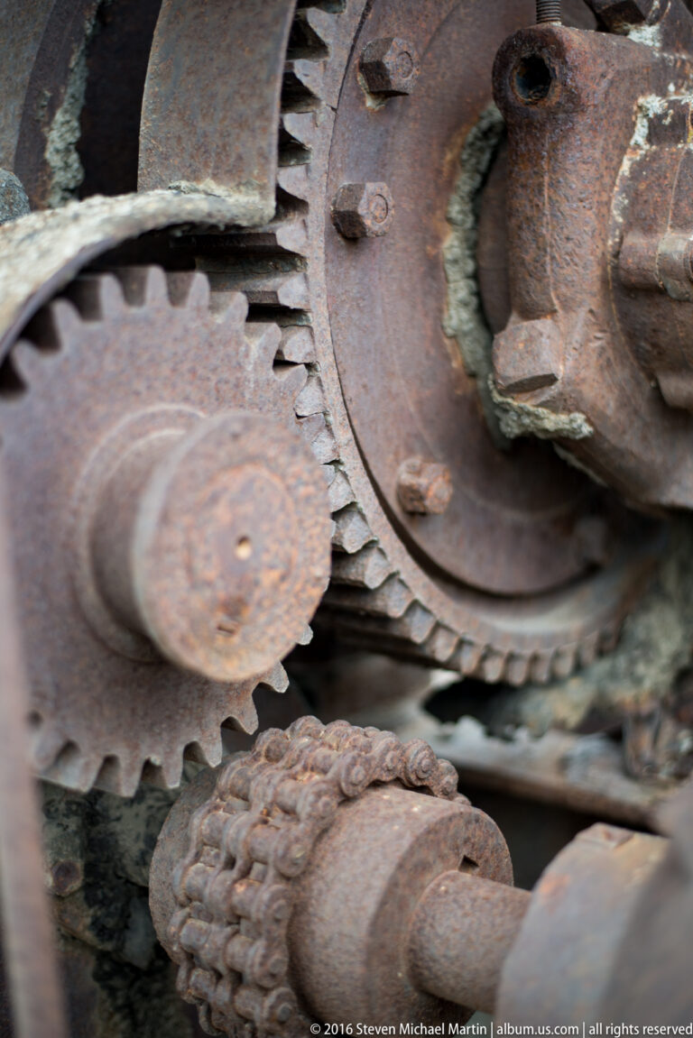 Two rusted toothed wheels meet beside a large circular plate secured with bolts.
