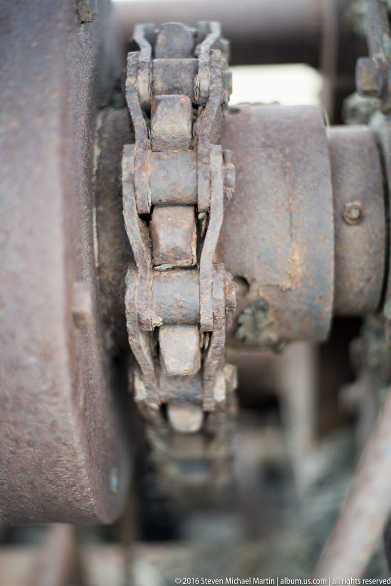 A thick rusted chain wraps around a shaft between two large cylindrical machine parts.