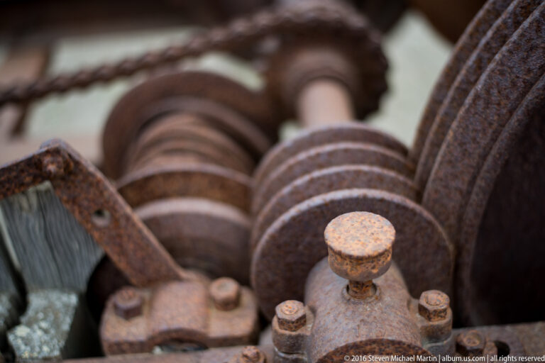 A row of rusted cylindrical rollers and round fasteners recedes through a machine.