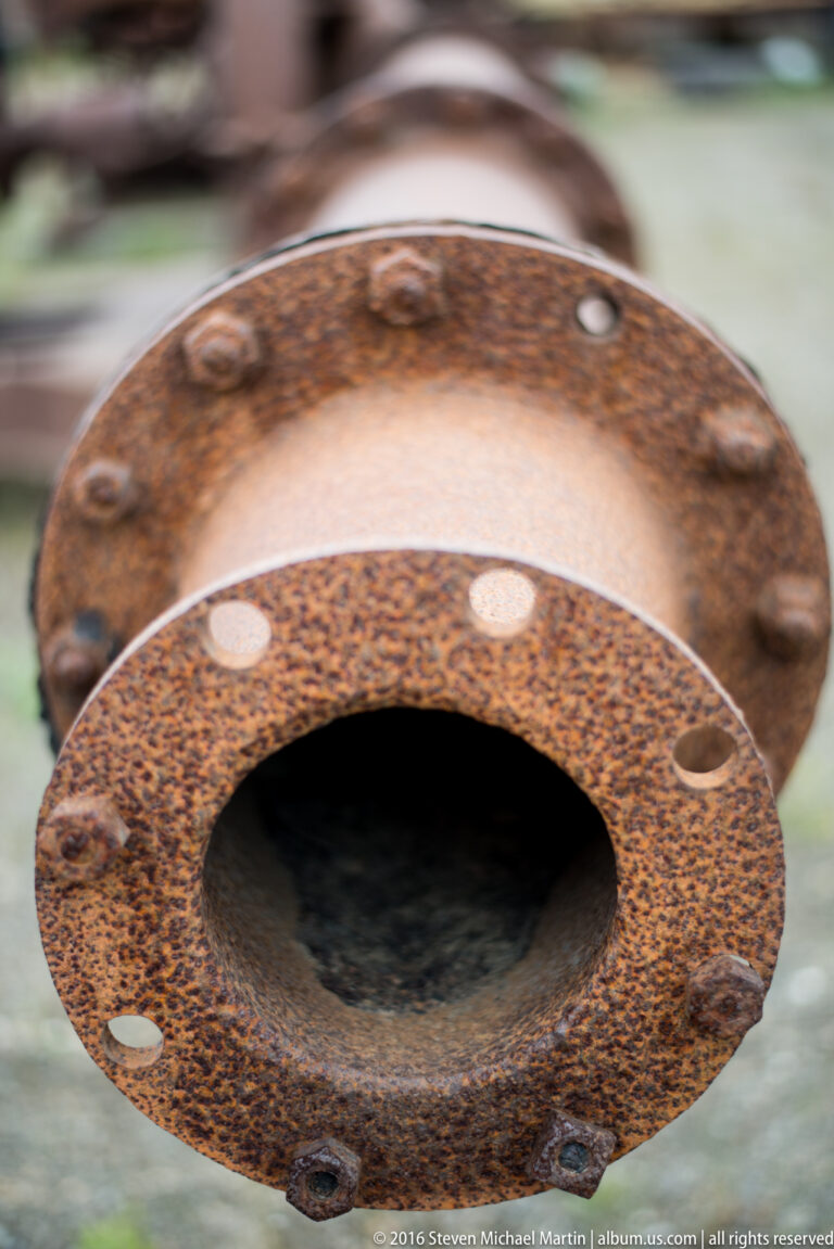 A rusted circular flange with a dark central opening and evenly spaced bolt holes fills the frame.