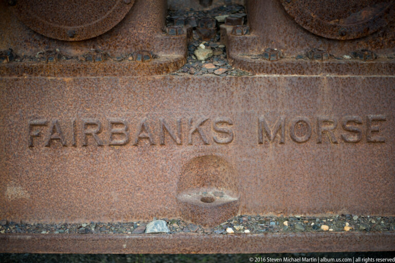 “FAIRBANKS MORSE” is cast into a rusted metal panel above a small round fitting.