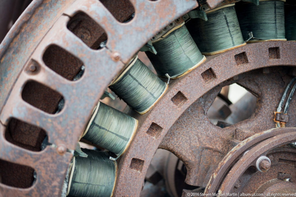 Wire coils sit between rusted perforated rings inside a circular machine frame.