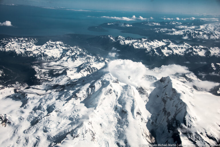 A steep snowy ridge fills the foreground as a higher peak rises above a bank of clouds.