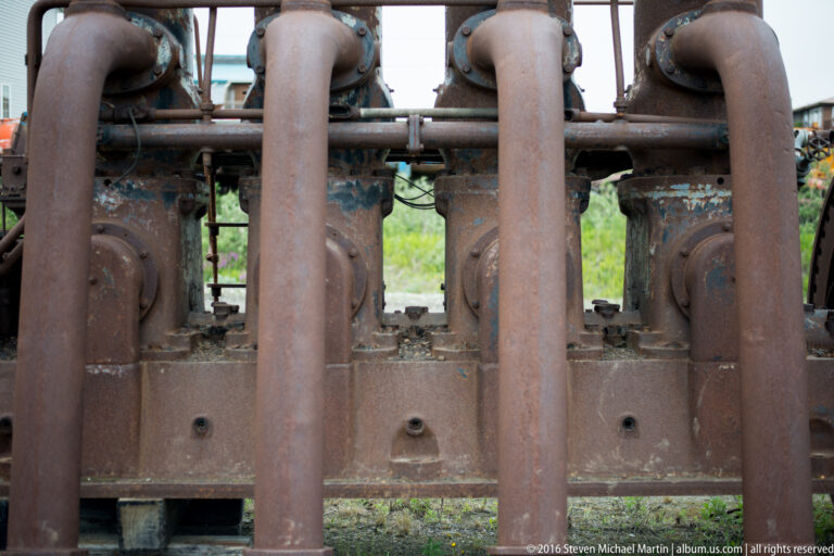 Several thick curved pipes hang from a horizontal bar in front of an old machine.