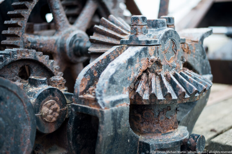 A large rusted toothed gear meshes with smaller cast-metal parts in a close view of old machinery.