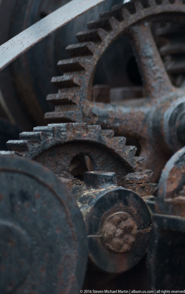 Rusted gear wheels overlap, with their teeth meshing across the center of the frame.