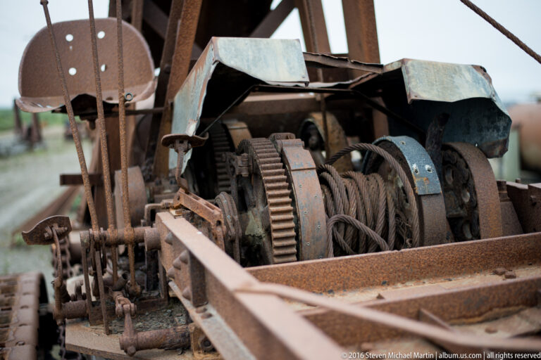 Rusted gears, coiled cable, supports, and metal guards fill the open frame of an old machine.