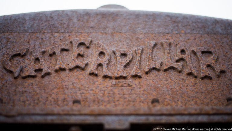 Blurred raised letters cross a curved rusted housing; corrosion obscures most of the mark.