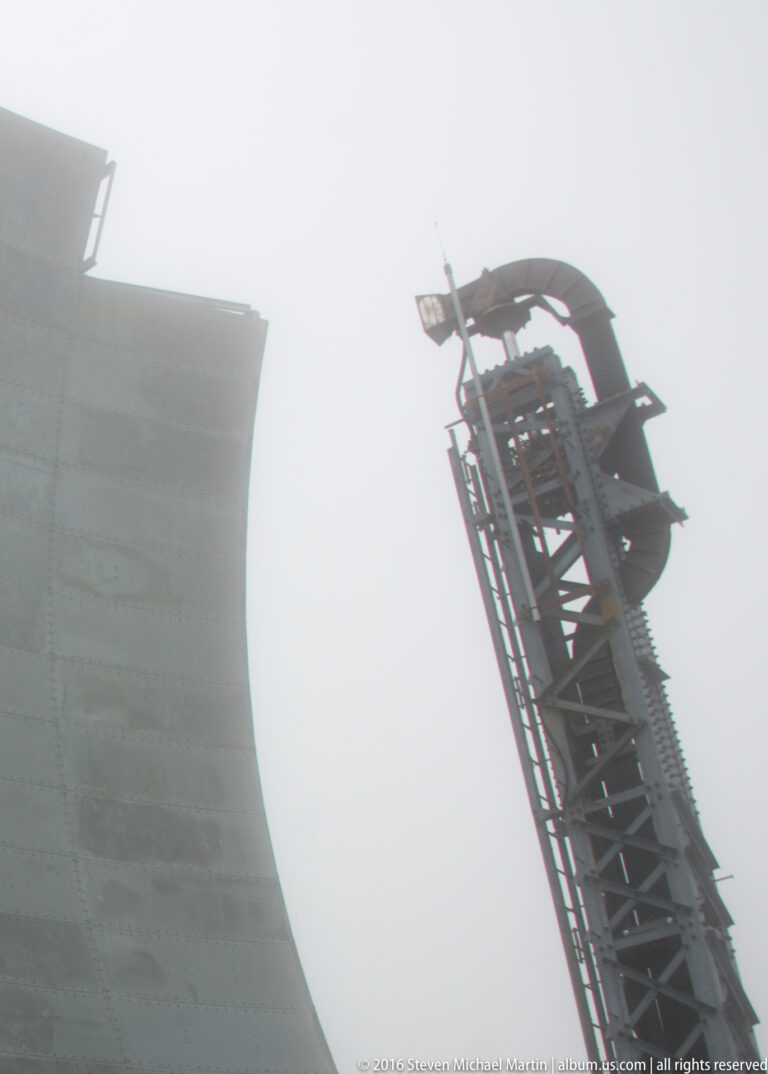 A tall lattice assembly rises beside the curved reflector of a White Alice antenna in bright haze.