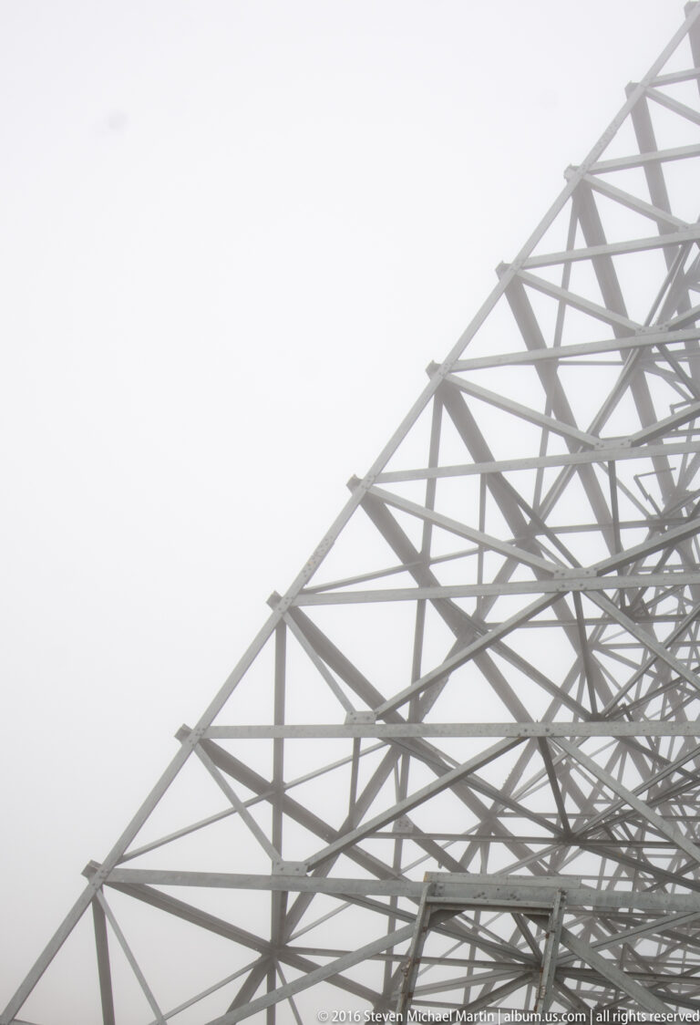 Triangular steel braces rise beside the edge of a White Alice reflector.