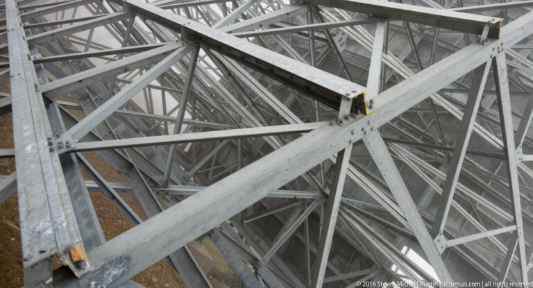 Steel beams and diagonal braces intersect beneath a White Alice reflector, forming a dense truss.