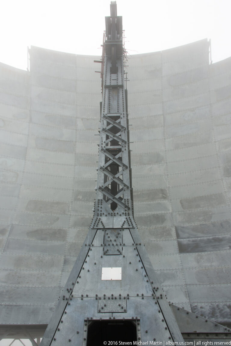 A central lattice feed structure stands before a broad curved White Alice reflector in fog.