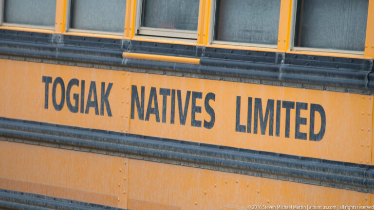 Large dark letters reading “TOGIAK NATIVES LIMITED” span the orange side of a vehicle below its windows.