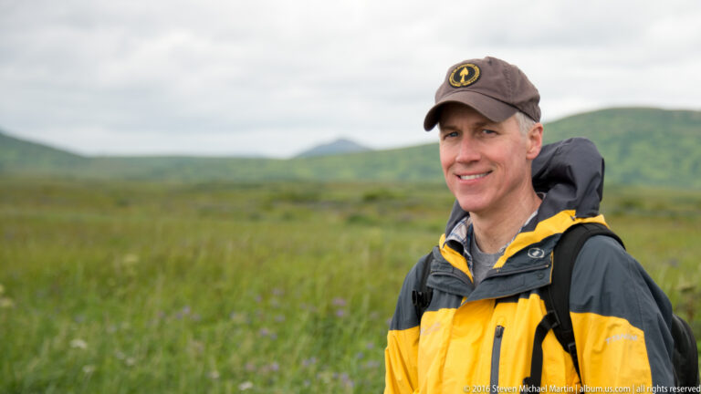 A closer portrait shows a smiling visitor in a dark cap and outdoor jacket against a blurred green meadow.