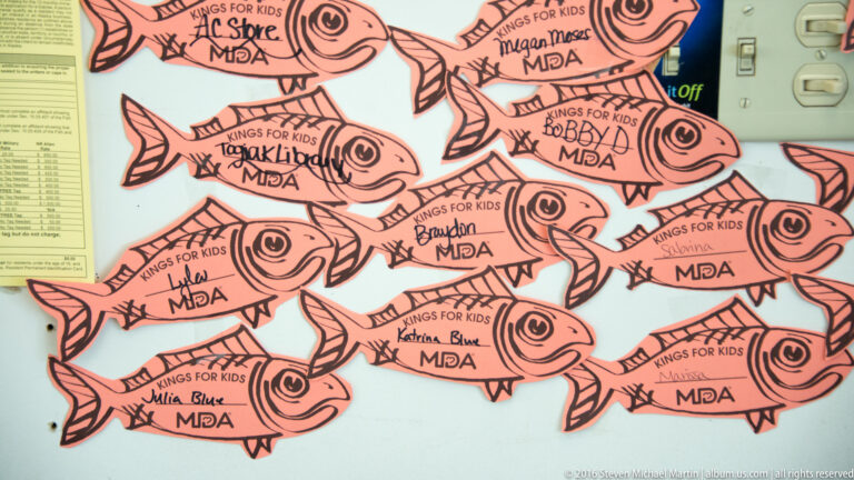 Orange salmon-shaped cards with handwritten names cover a board beside an MDA logo and electrical controls.