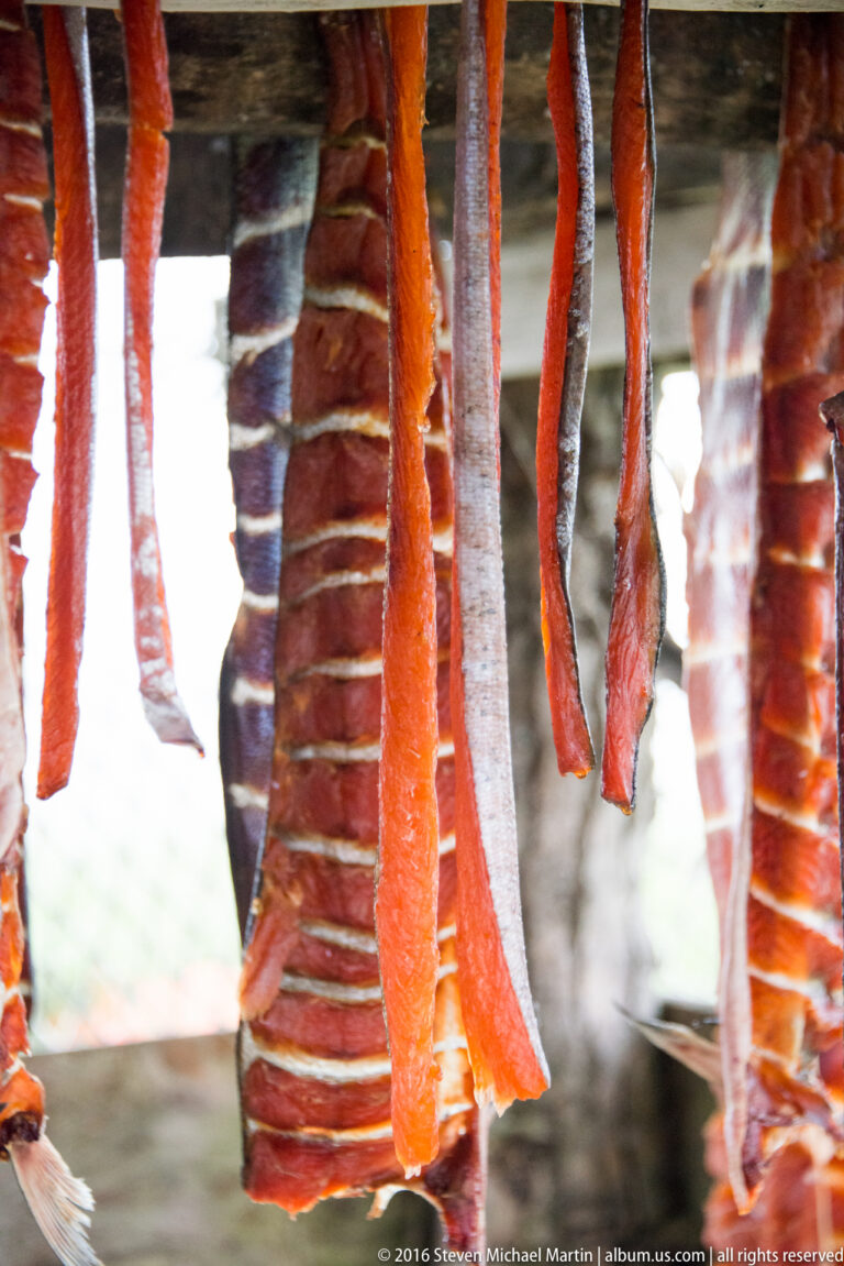 Split fish strips hang close together, exposing orange flesh, pale ribs, and dark skin.