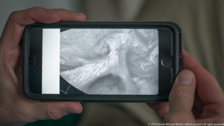 Hands hold a smartphone showing a blurry grayscale image with indistinct shapes and faint lines.