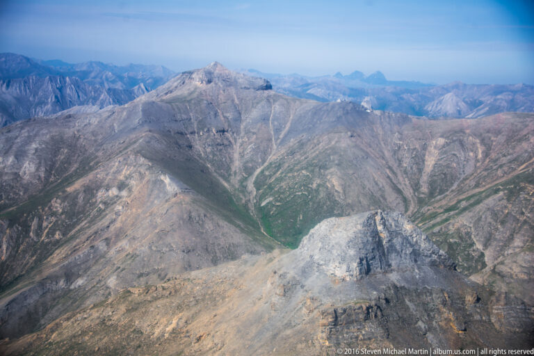 Pale rocky ridges and green valleys spread across a wide mountain panorama beneath a blue horizon.