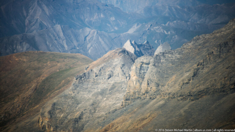 Distant pale twin pinnacles appear between brown foreground ridges and dark mountain walls.