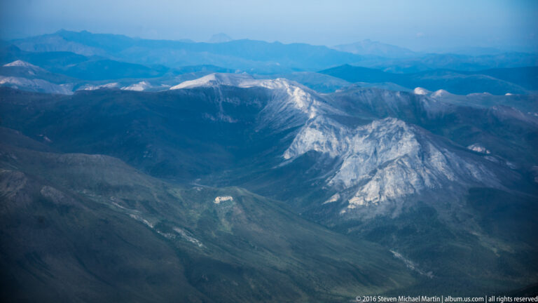 A pale mountain mass with branching channels rises above a shadowed valley and hazy blue ridges.