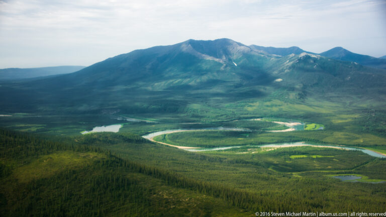 A pale river winds through a wide green valley beneath a rounded mountain and open tundra.