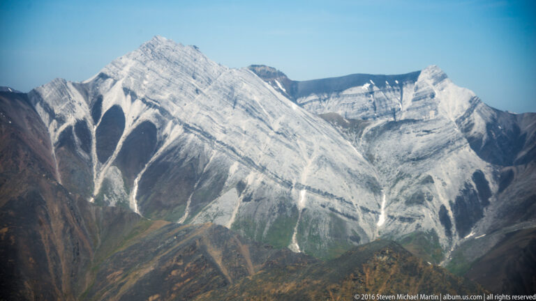 Pale gray peaks with deep vertical gullies and lingering snow rise above rust-colored foothills.