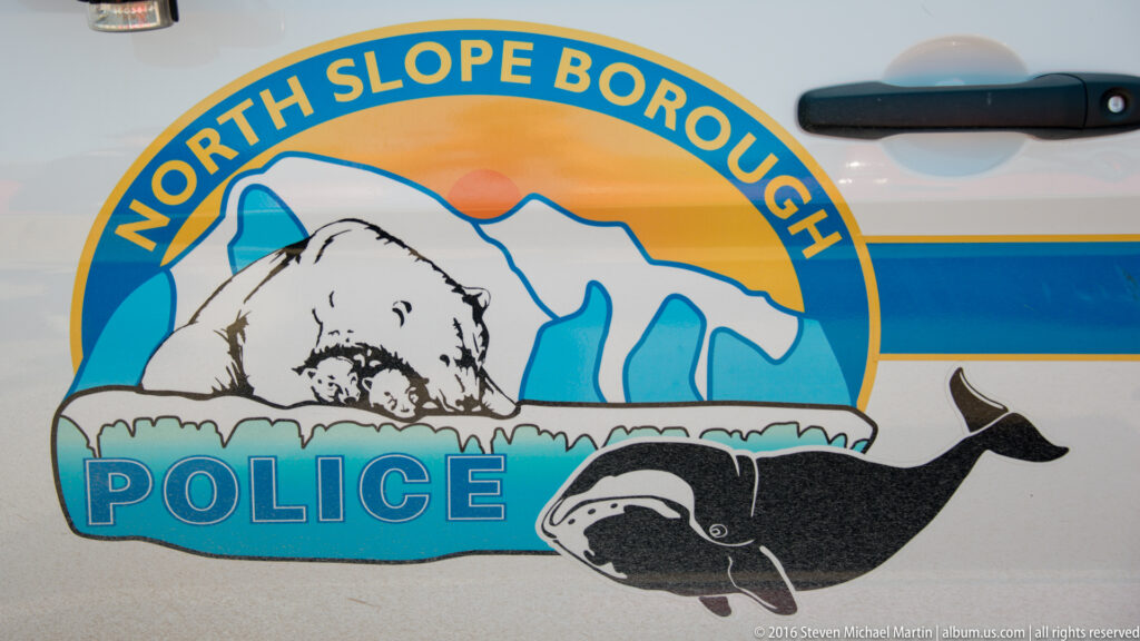Close view of a North Slope Borough Police emblem, with a polar bear, Arctic landscape, and whale graphic on a white aircraft fuselage.