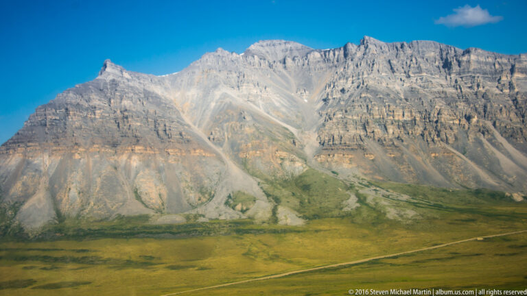 A long pale mountain wall rises above a broad green valley floor.